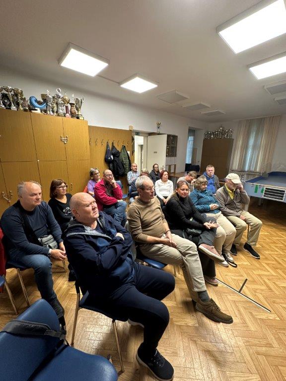 Slika prikazuje člane, ki poslušajo pripovedovanje gostov.