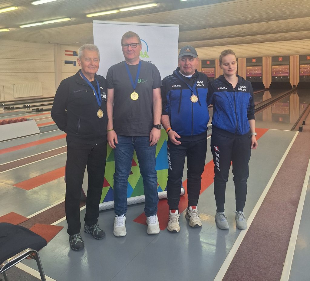 Na fotografiji so prikazani trije nagrajenci v kategoriji B2, ki stojijo drug ob drugem. Od leve proti desni so: Jože Lampe, ki je osvojil drugo mesto, Igor Žagar na sredini kot zmagovalec s prvim mestom, ter Ladislav Humski na desni, ki je osvojil tretje mesto. Ob njih stoji tudi predsednica MDSS Celje, Sanja Kos, ki se jim je pridružila ob podelitvi priznanj.